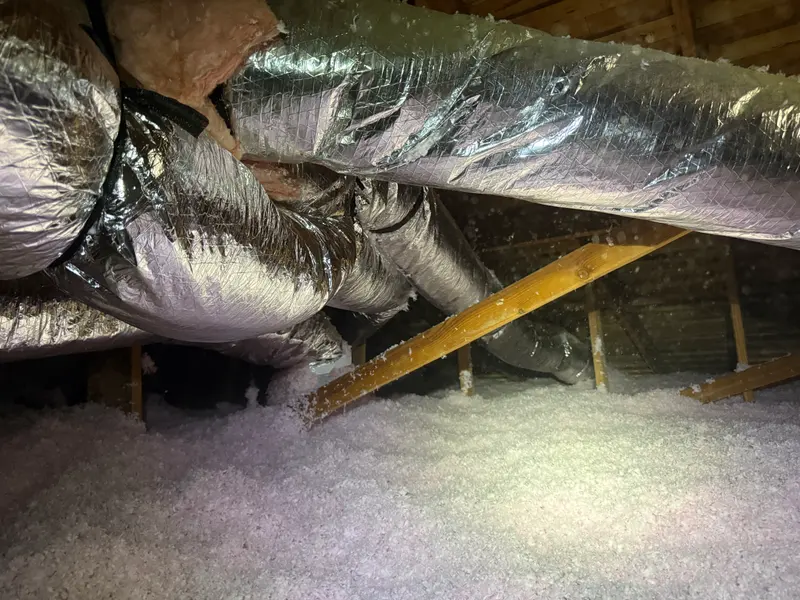 Insulated flex ductwork running through an attic above blown-in insulation
