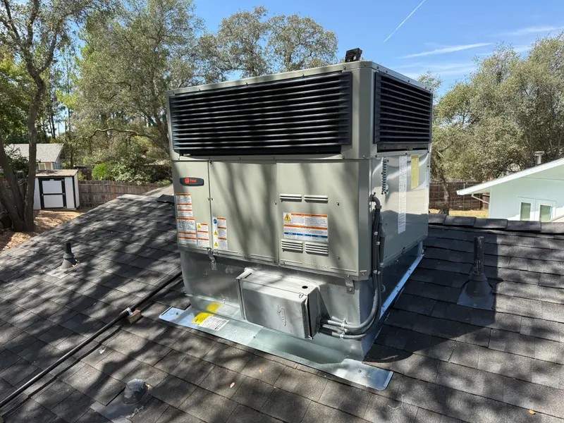 New rooftop package HVAC unit installed on a shingle roof under trees
