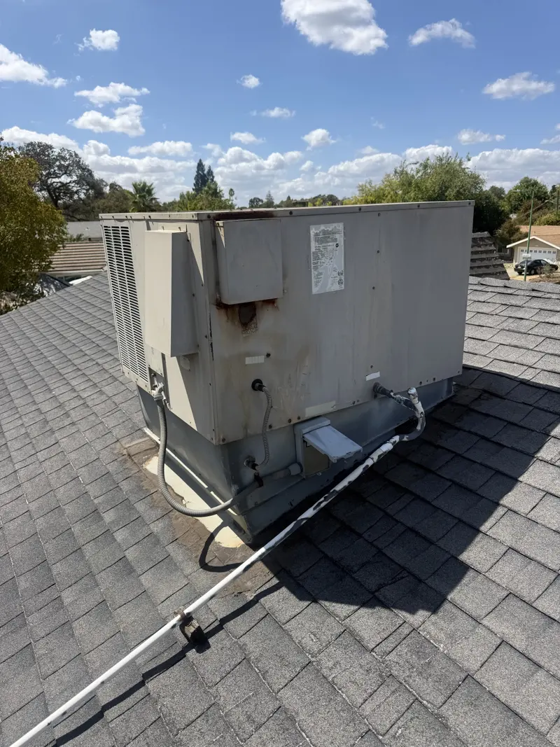 Old rusted rooftop package HVAC unit on a shingle roof before replacement